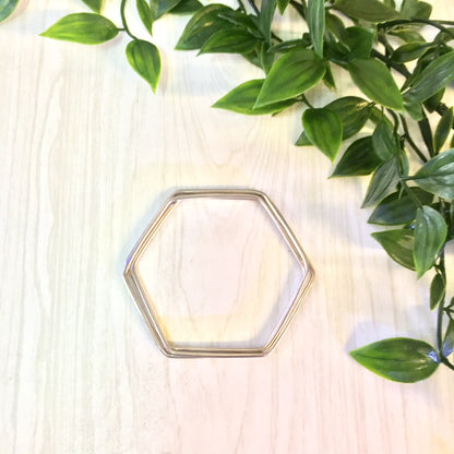 Vintage silver hexagon bangle bracelet with three interlocking pieces on wooden surface surrounded by green leaves