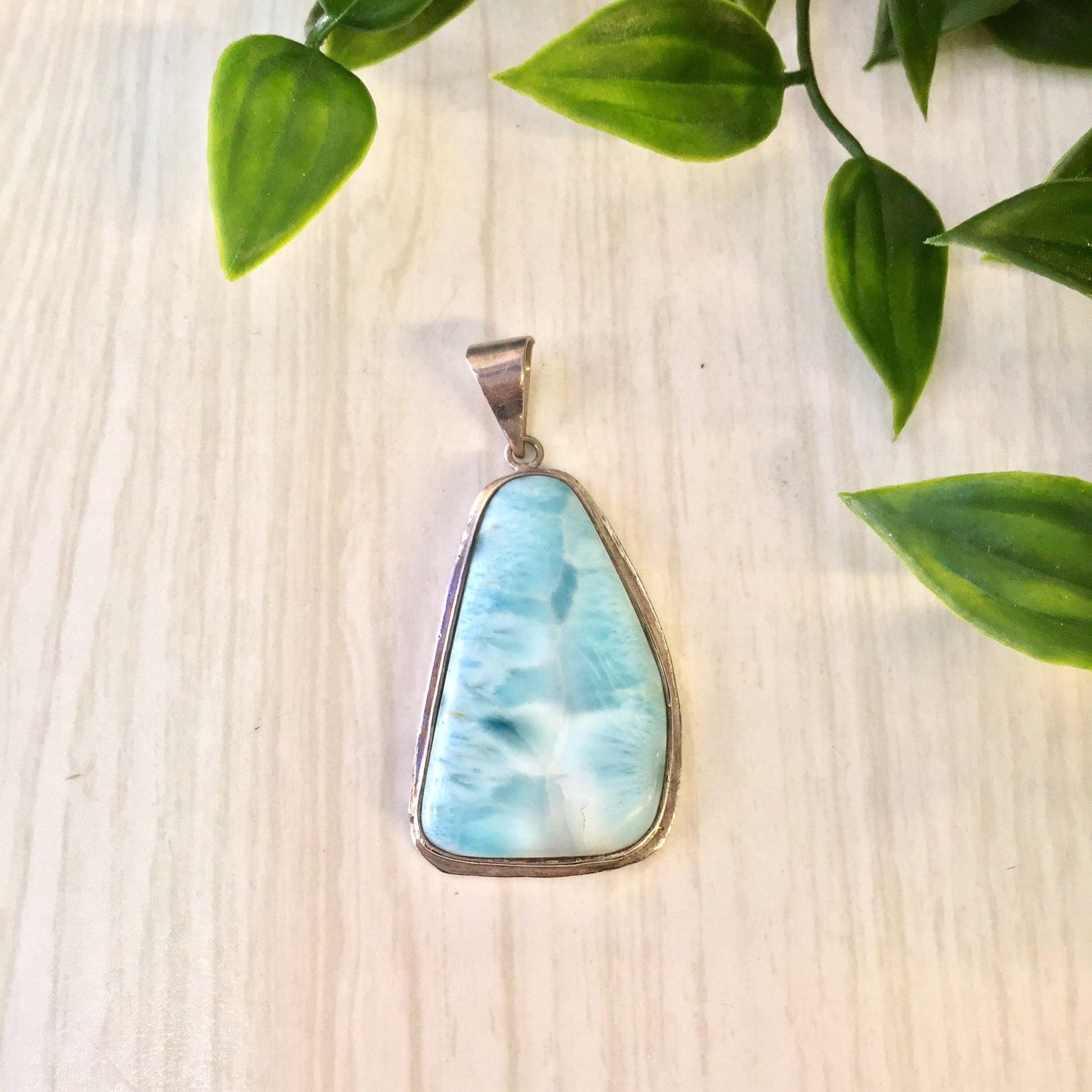 Vintage silver and larimar pendant necklace with blue and white natural stone against wooden background with green leaves