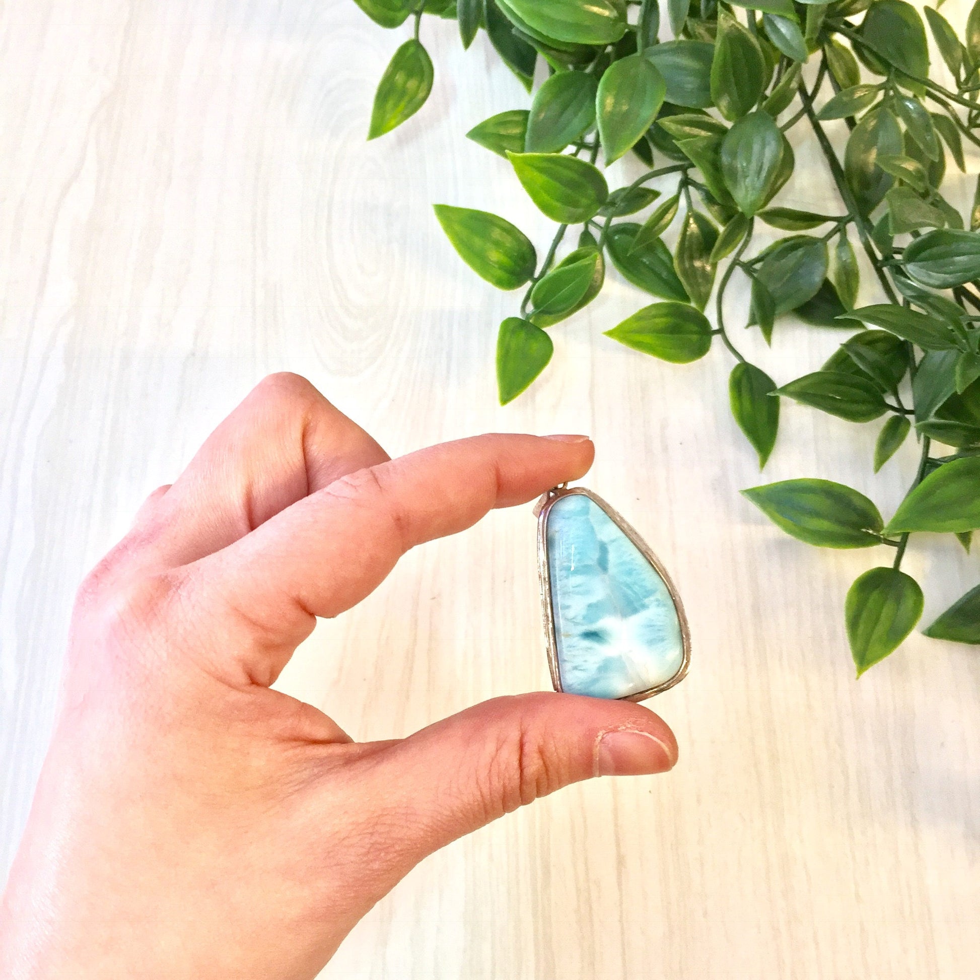 Hand holding vintage silver pendant with blue larimar natural stone against green leafy plant background