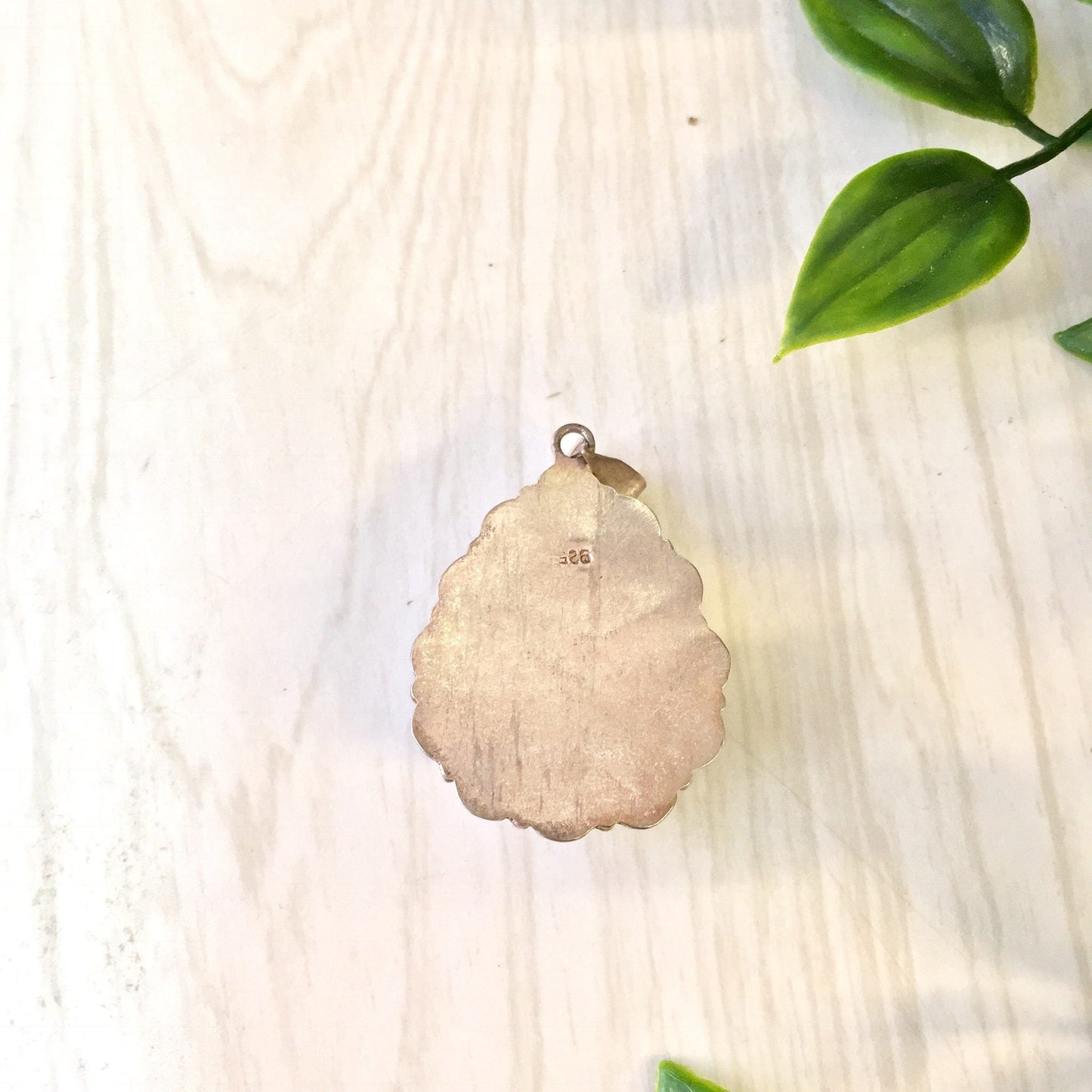 Vintage sterling silver pendant with an opalite gemstone displaying shimmering blue and green hues, placed on a light wooden surface with green leaves.