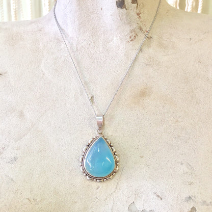 Vintage sterling silver pendant necklace with blue-green opalite gemstone on textured light background.
