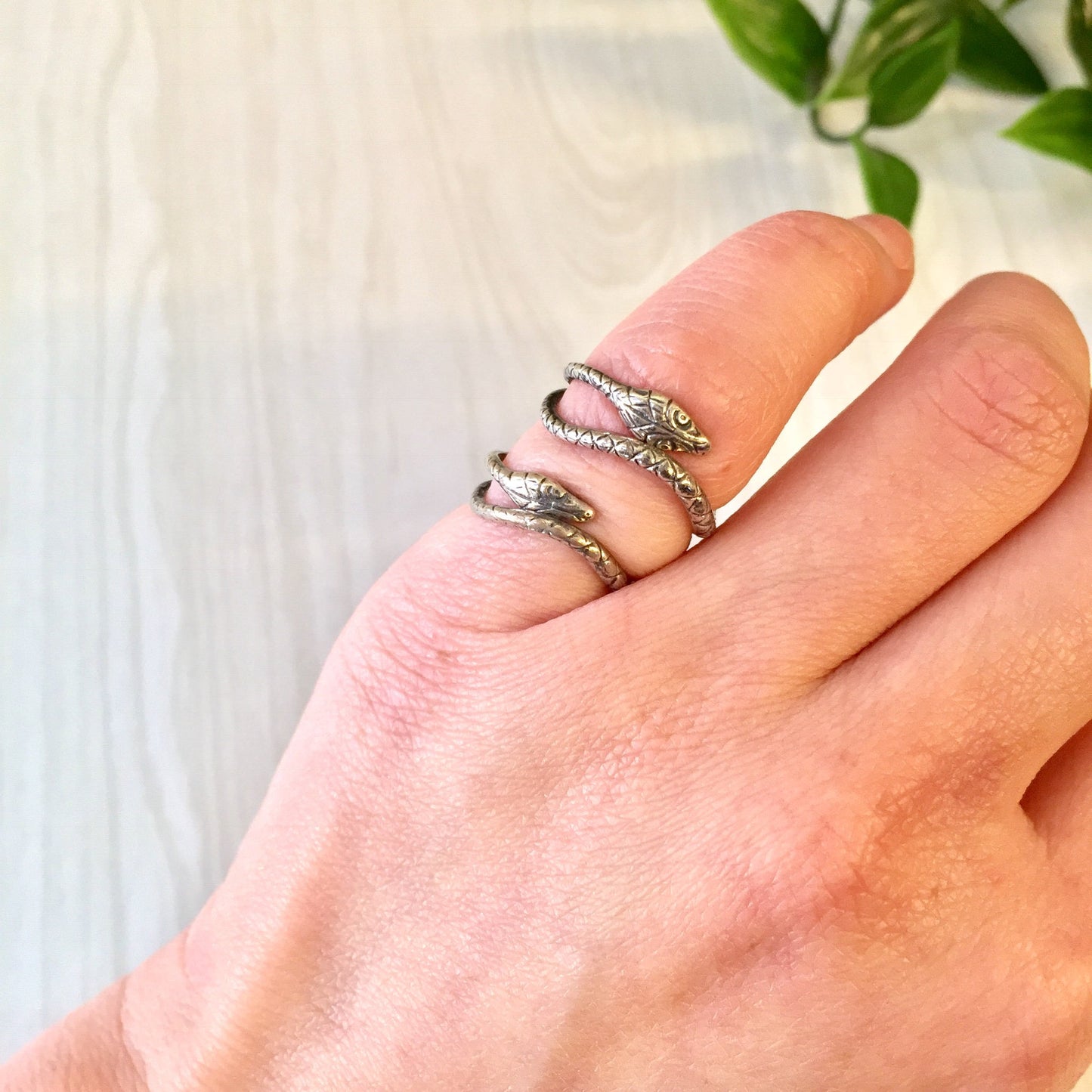 Vintage silver snake ring on a person's finger, with green leaves in the background. Boho statement jewelry makes a stylish gift for her or unique hippie accessory.