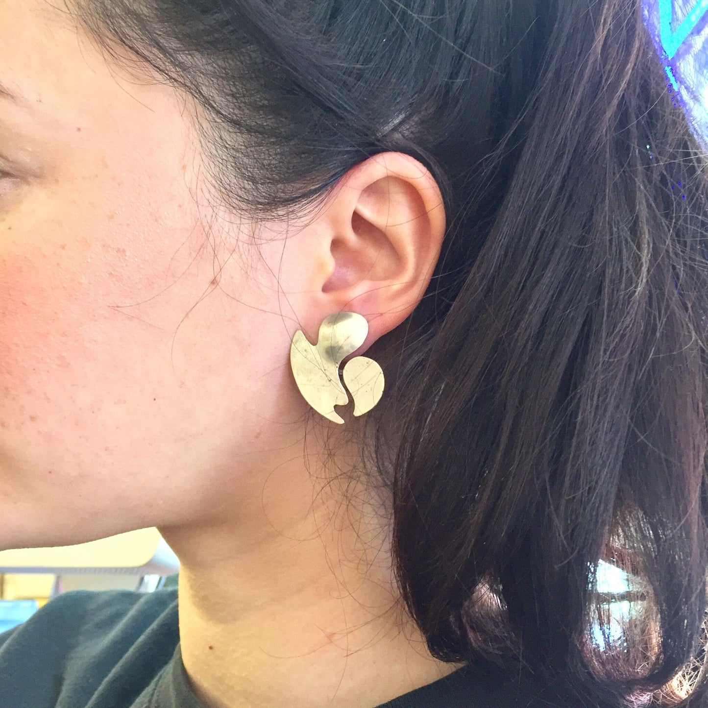 Close-up view of a woman's ear wearing a vintage abstract sterling silver earring resembling a flower or leaf shape, with her long dark hair visible.