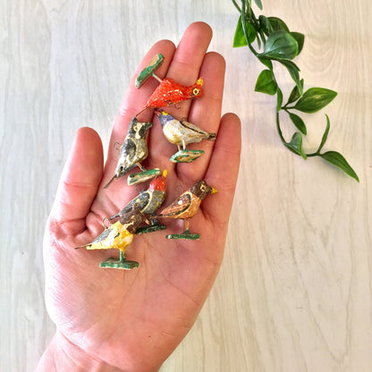 Colorful handmade paper mache bird beads in red, yellow and brown held in palm for jewelry making or arts and crafts projects.