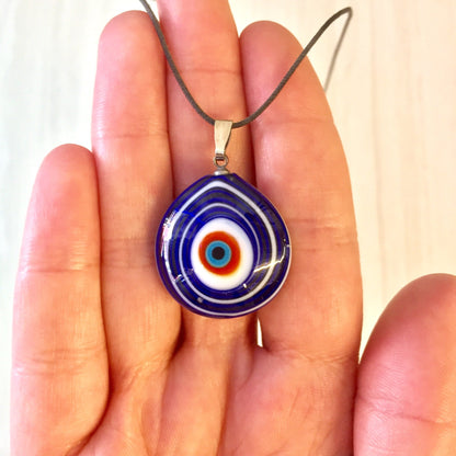 Blue and white bullseye evil eye glass pendant necklace held in a person's hand against a plain background.