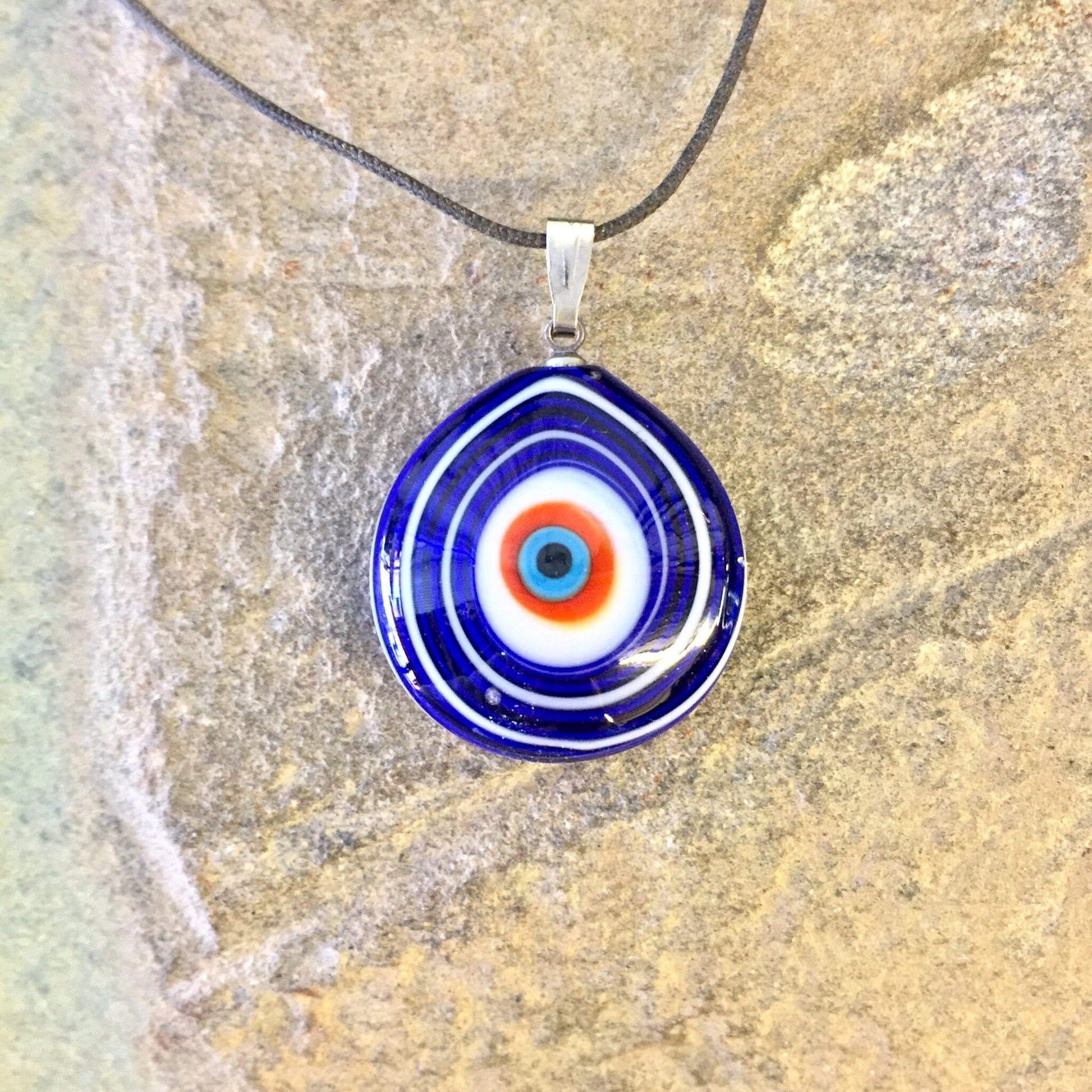 Vintage blue, red and white evil eye glass pendant necklace on black cord against textured stone background