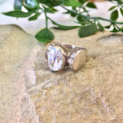 Vintage sterling silver statement ring with oval moonstone and diamond accents, presented on stone surface with greenery in background