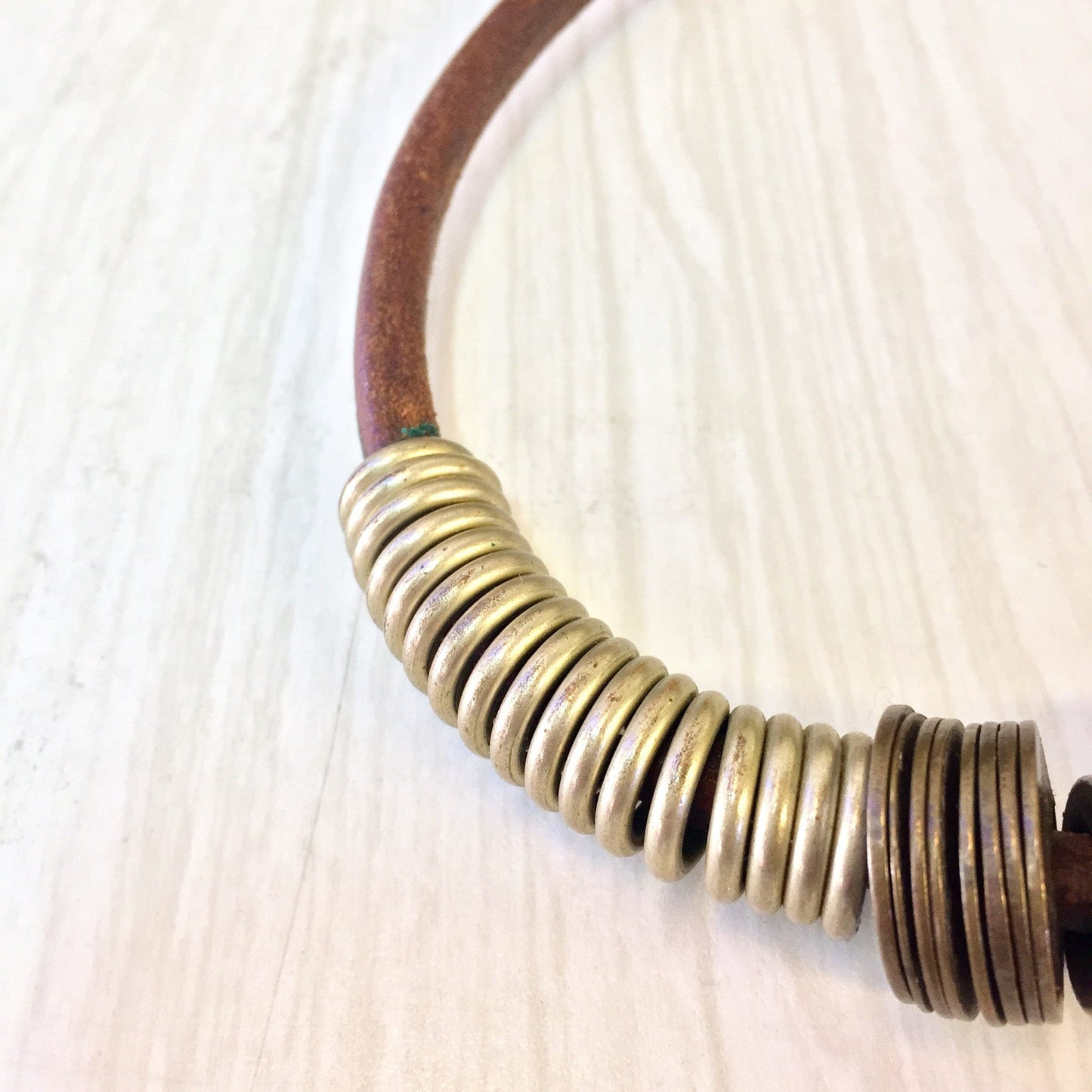 Vintage leather and brass coil choker necklace on light wooden surface, unique ethnic statement jewelry perfect for a Mother's Day gift.