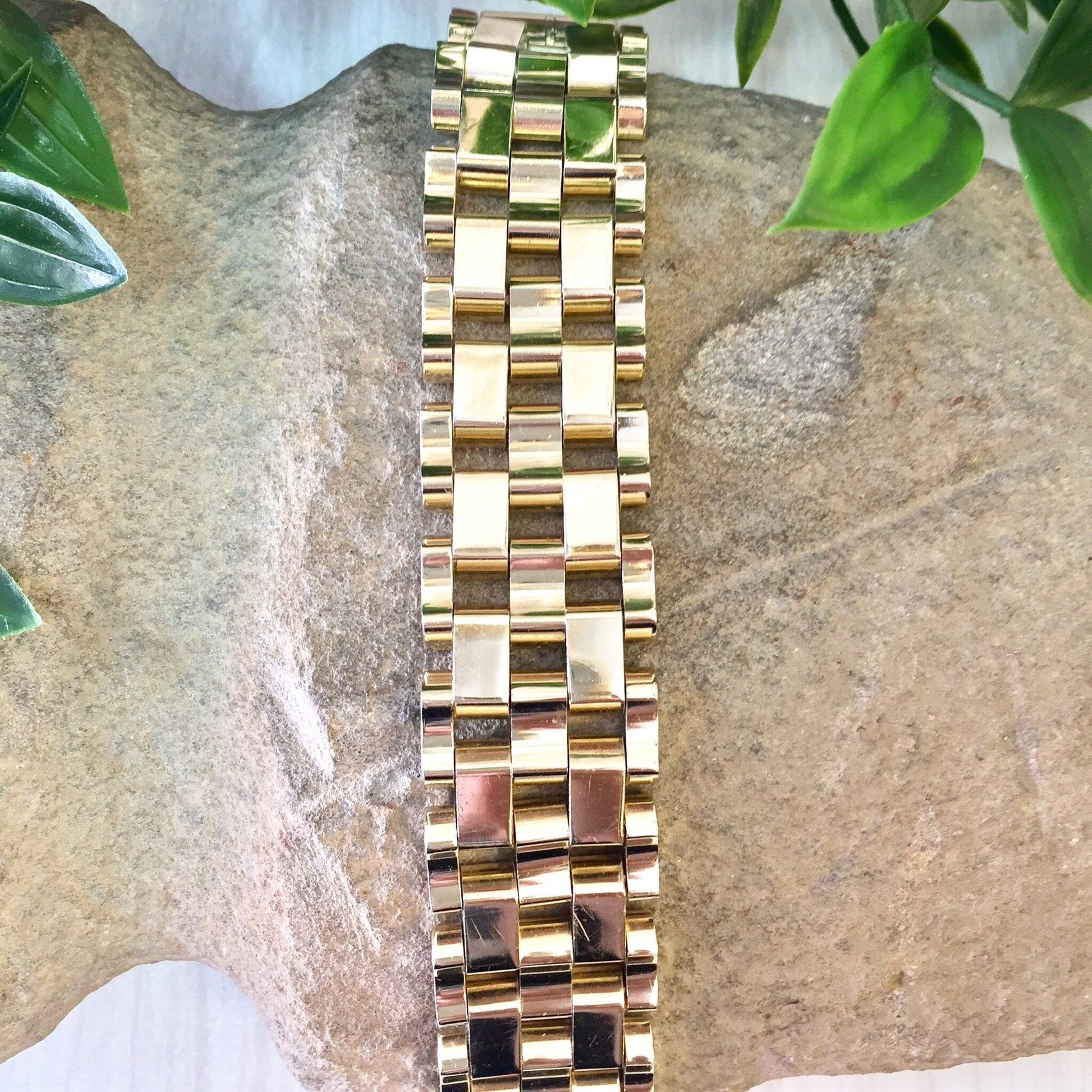 Vintage gold-toned chunky chain link bracelet, suitable as a gift for mom, displayed on a stone surface with green leaves in the background.