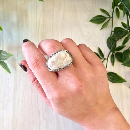 Vintage sterling silver ring with large, hammered rope setting showcasing a statement quartz stone against a light wood background with green leaves.