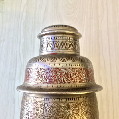 Vintage etched metal cocktail shaker with intricate silver and red floral design, Indian-inspired barware for mixology enthusiasts.