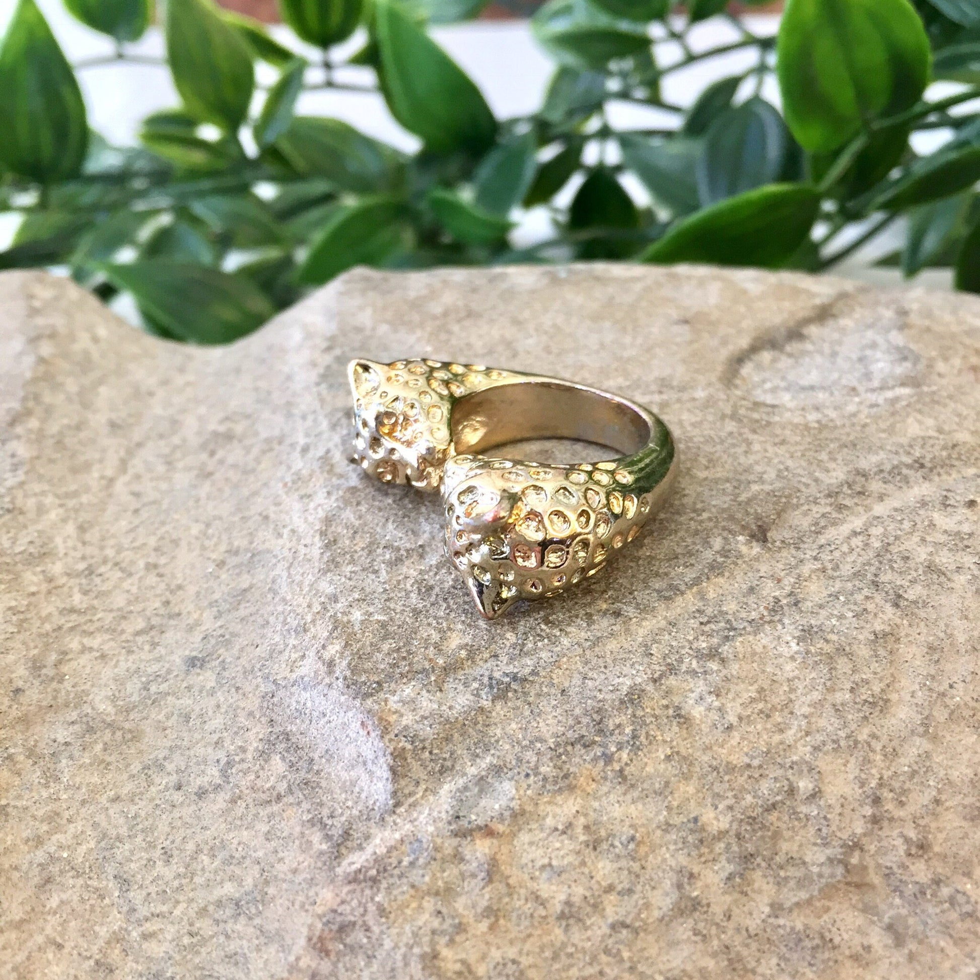 Vintage gold tone double leopard head ring displayed on a rock with greenery in the background