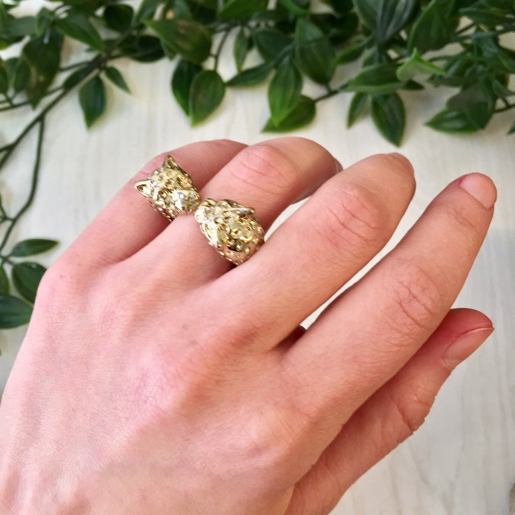 Vintage gold tone double leopard head statement ring displayed on a hand against a leafy green background