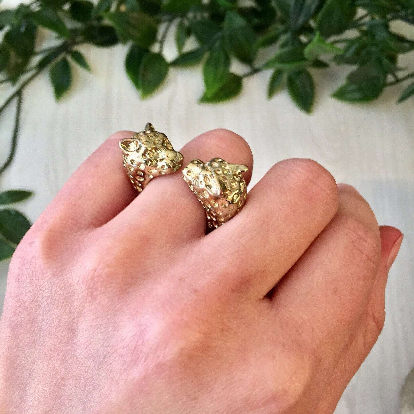 Vintage gold tone double leopard head statement ring displayed on hand with greenery in background