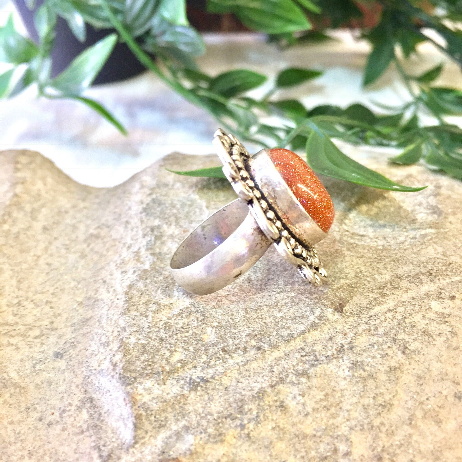 Vintage sterling silver ring with orange druzy quartz stone and Celtic design band, statement jewelry with sparkle, on rock surface with greenery in background