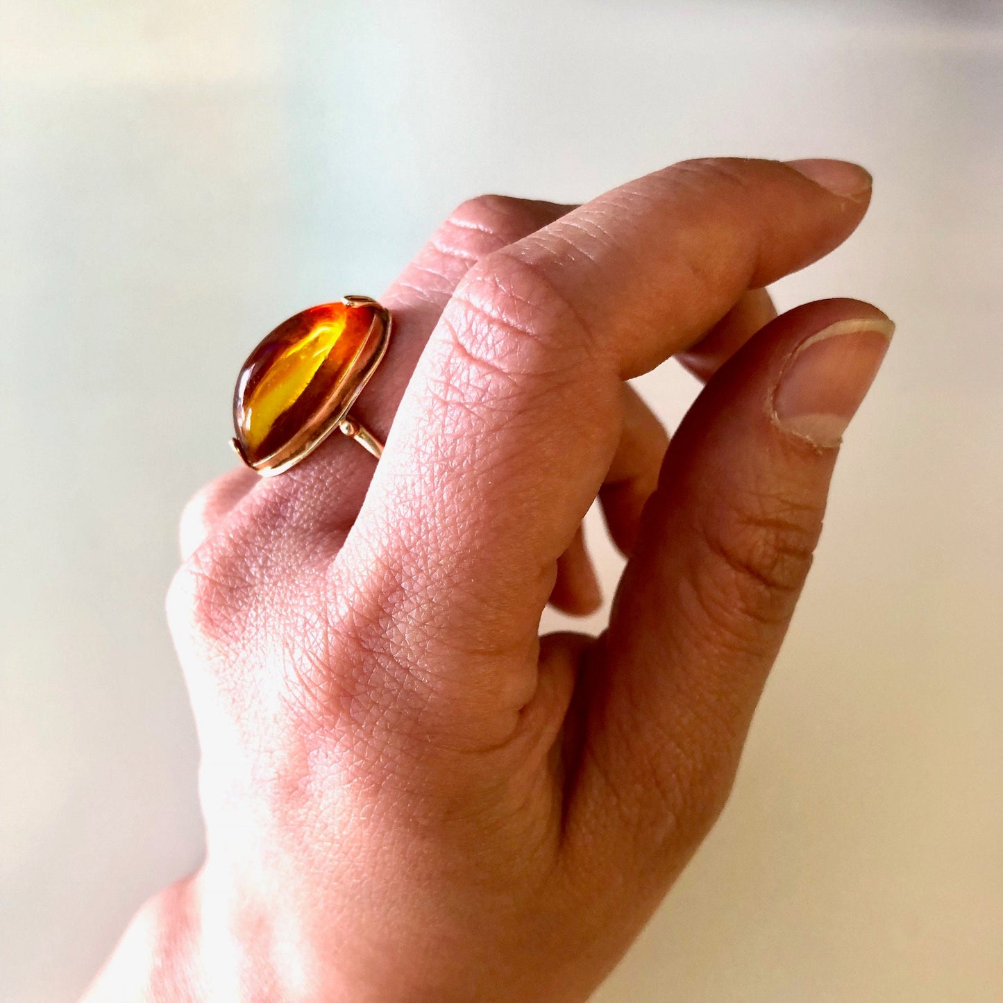 Vintage 10K yellow gold ring with an oval amber stone held between the fingers, displaying the ring's design and color against a plain background.