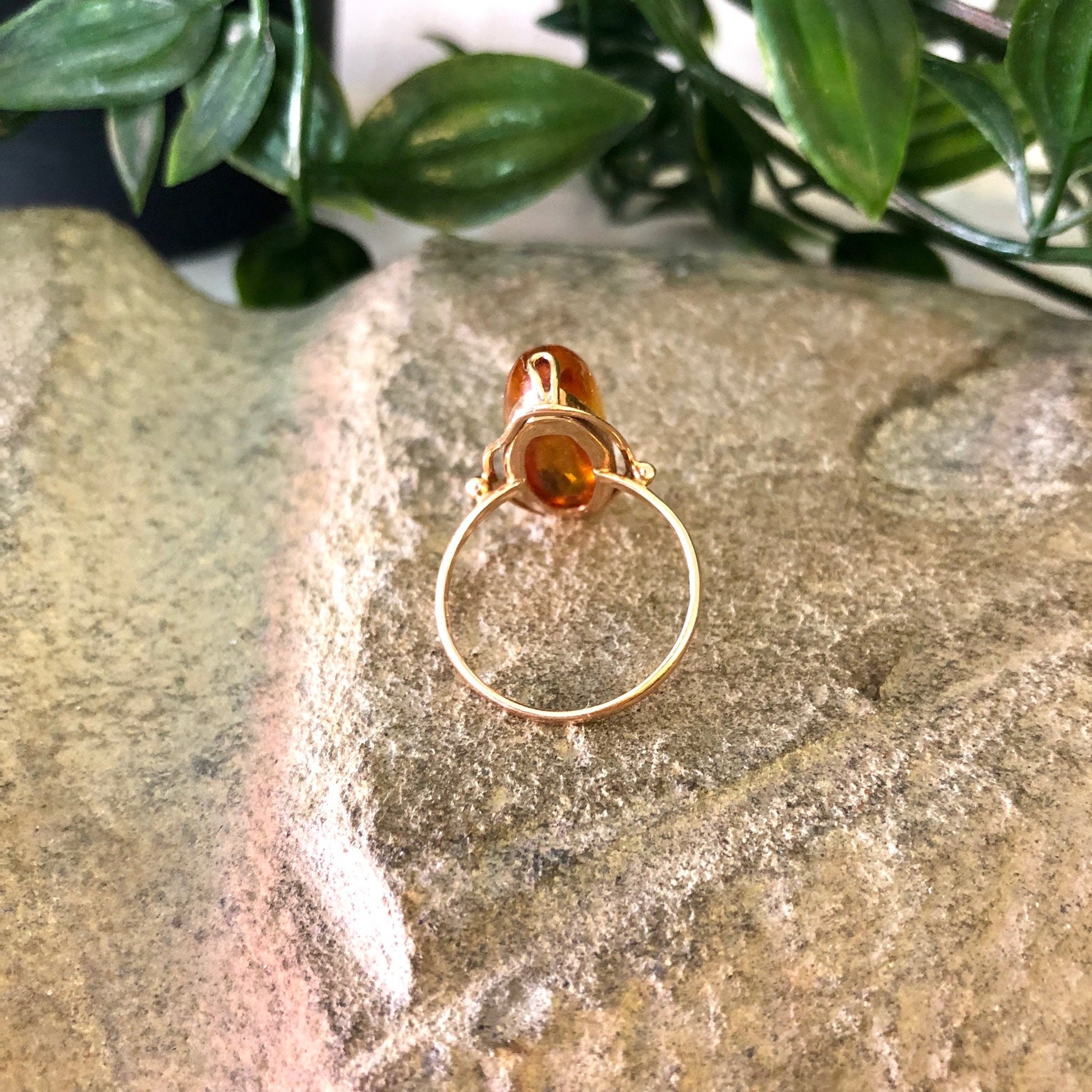 Vintage 10K yellow gold ring with an amber stone, placed on a stone surface with greenery in the background.