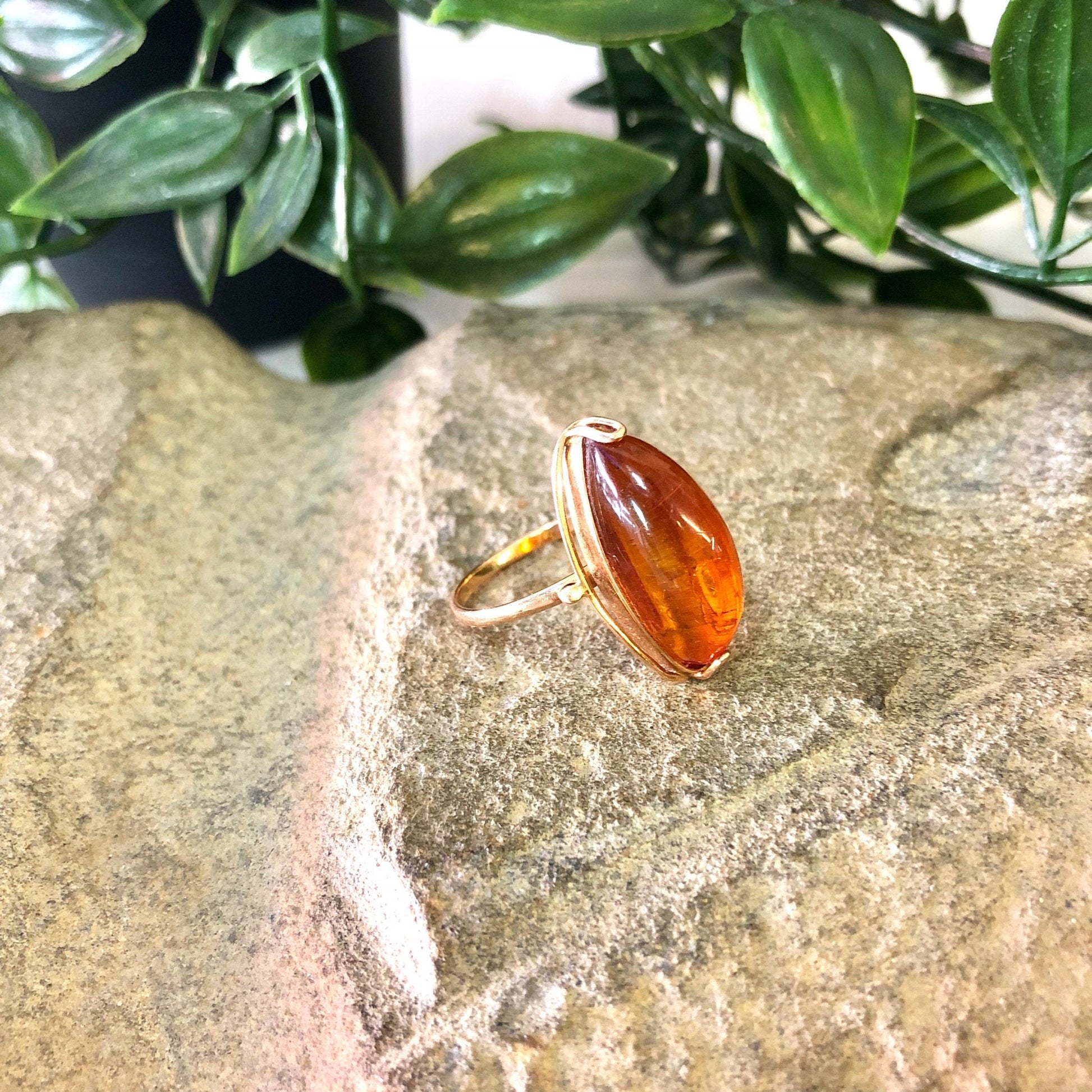 Vintage 10K yellow gold ring with an oval amber stone, resting on a stone surface with greenery in the background.