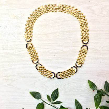 Vintage gold tone chain link statement necklace on white wooden surface with green leaves