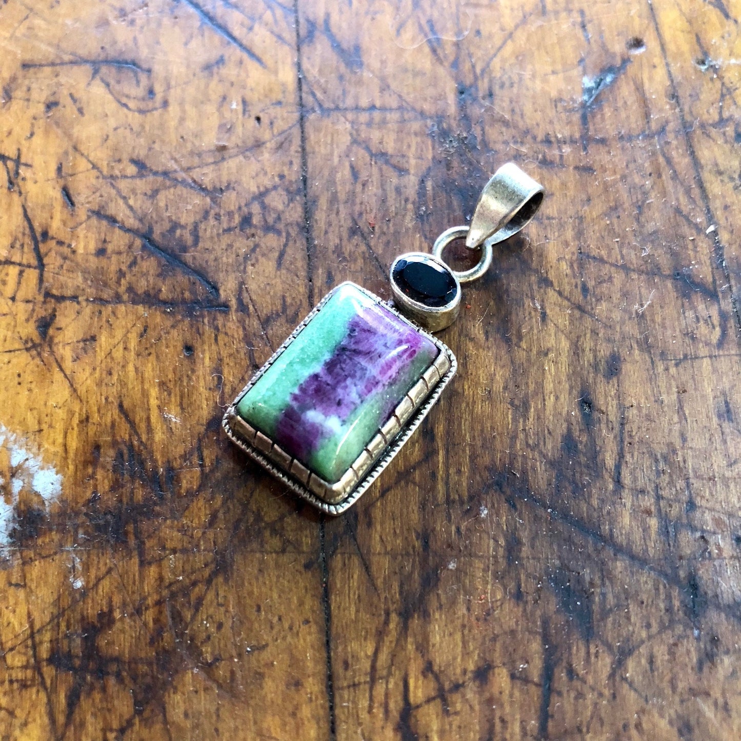 Vintage sterling silver pendant with green and purple natural stone and red garnet gemstone on a wooden surface