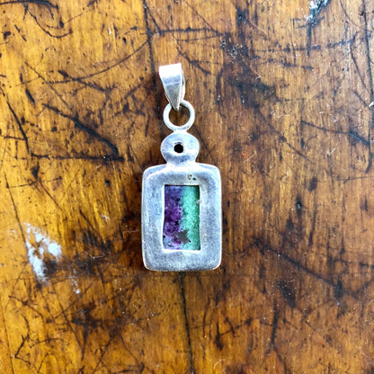 Vintage sterling silver pendant with green and purple natural stone inlay and red garnet gemstone, on a wooden surface.