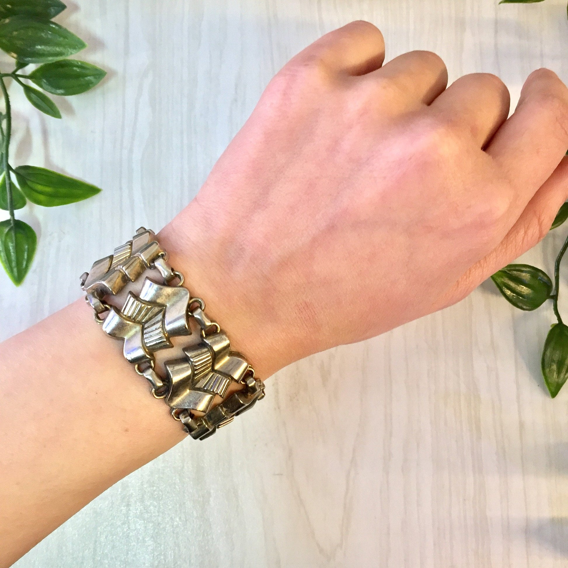 Vintage silver tone link bracelet on person's wrist next to plant leaves, costume jewelry statement piece, gift idea for mom.