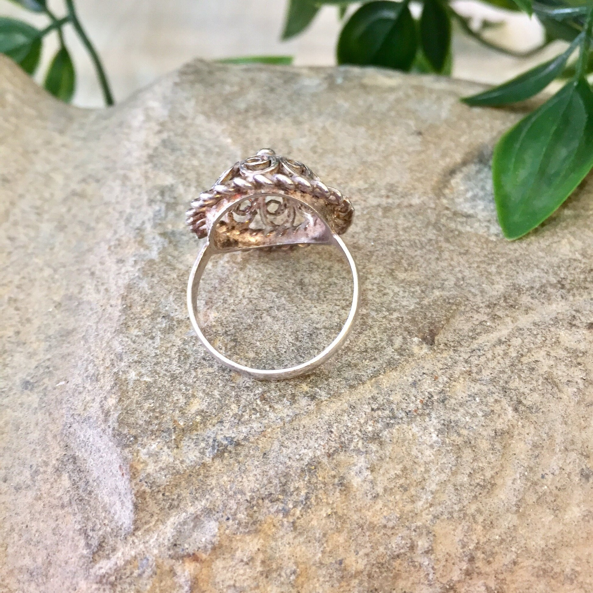 Vintage sterling silver dome ring with ornate cutout designs, displayed on stone surface with green foliage in background.