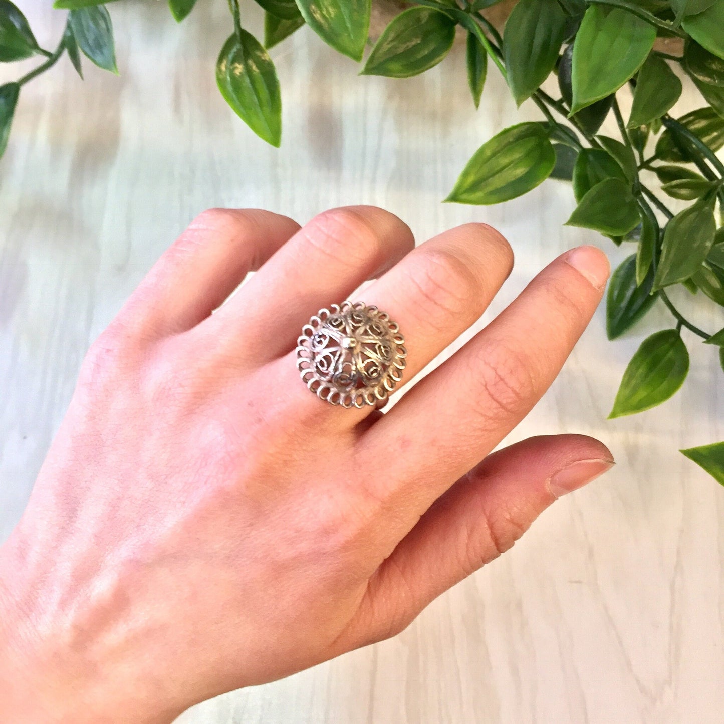 Vintage sterling silver bell-shaped dome ring with cut-out floral design, shown on a hand against a background of green leaves, perfect gift idea for Mother's Day or wedding jewelry.