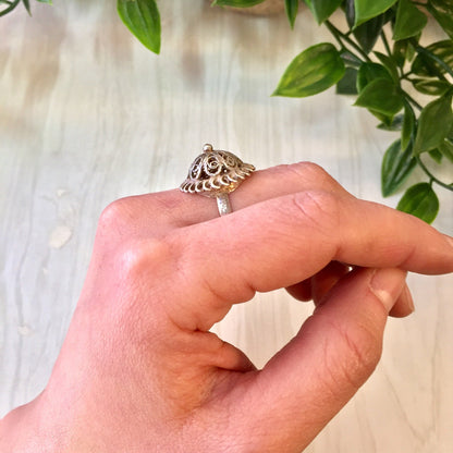 Vintage sterling silver dome ring with intricate cut-out design, held in front of green foliage, perfect gift idea for weddings, Mother's Day or vintage jewelry lovers.