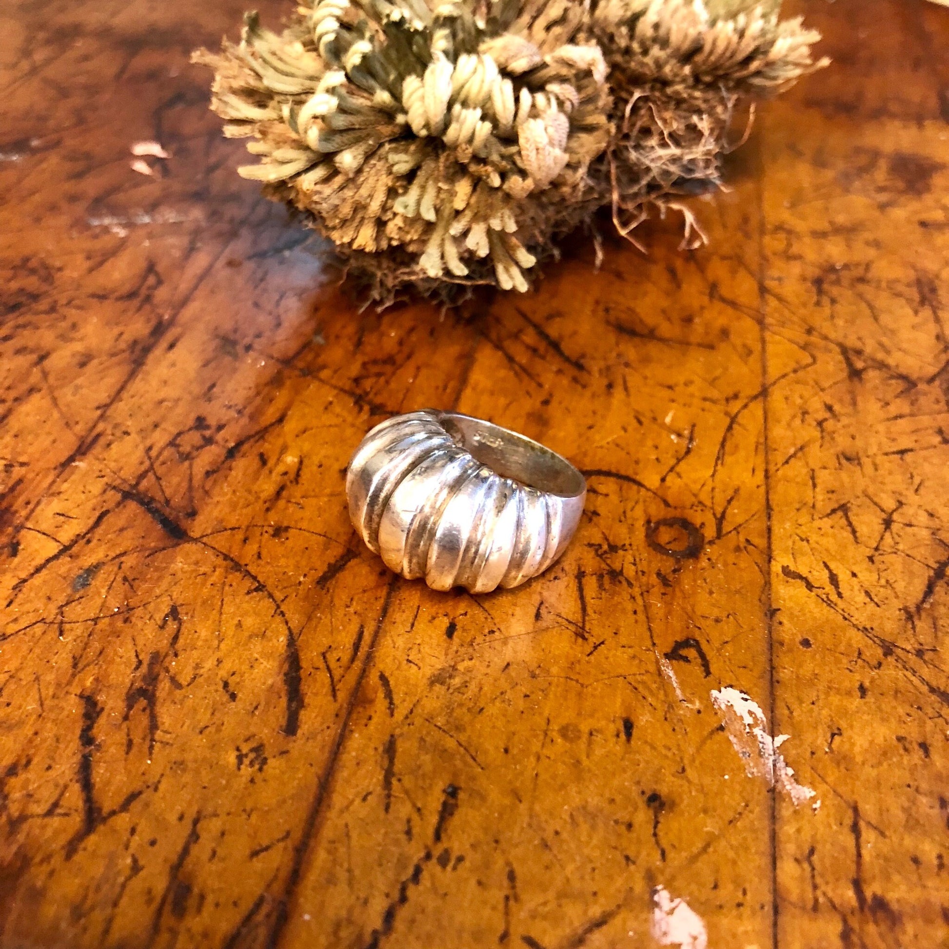 Vintage sterling silver statement ring with ridged design on rustic wooden surface next to dried flowers