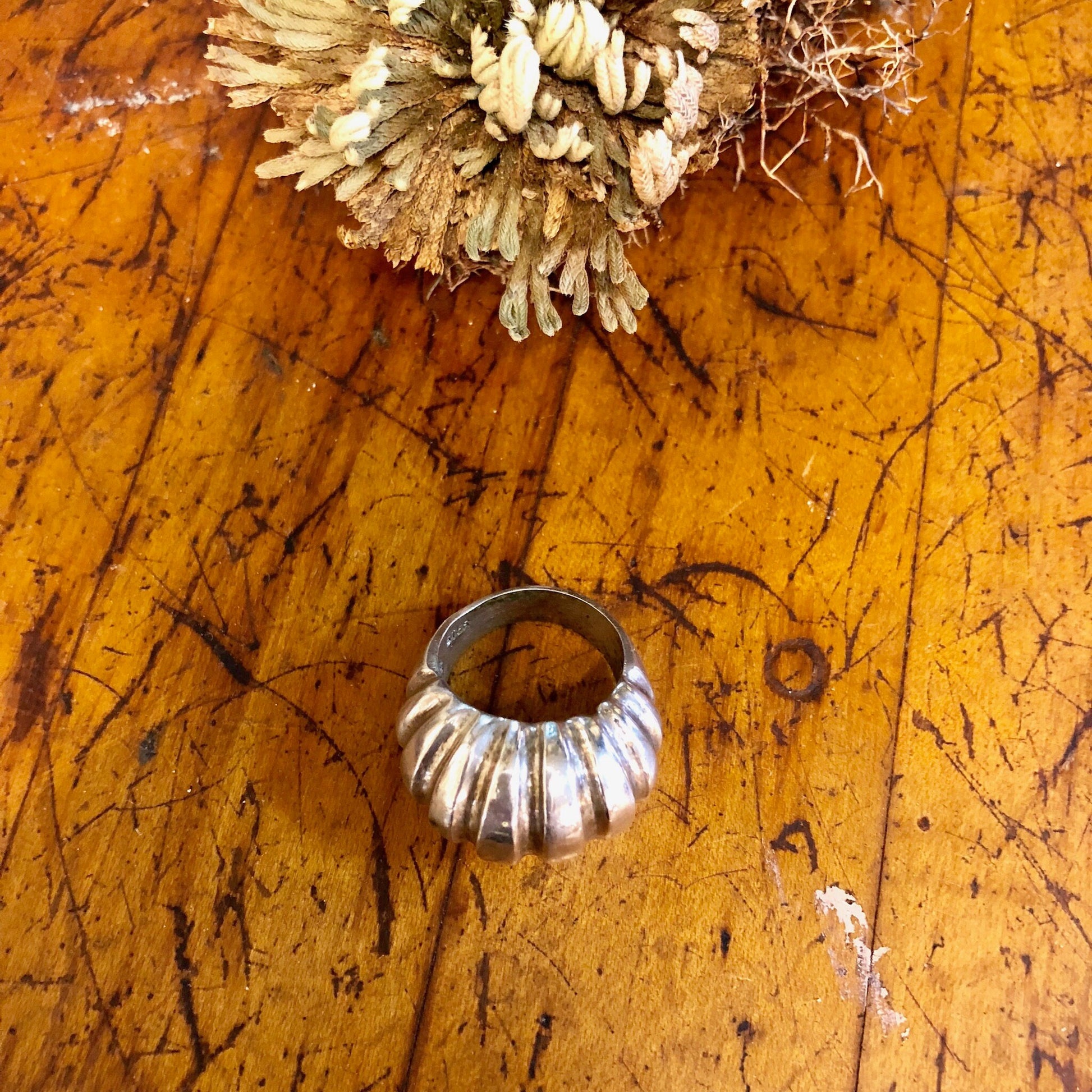 Vintage silver ridged statement ring on old wooden surface with dried flowers