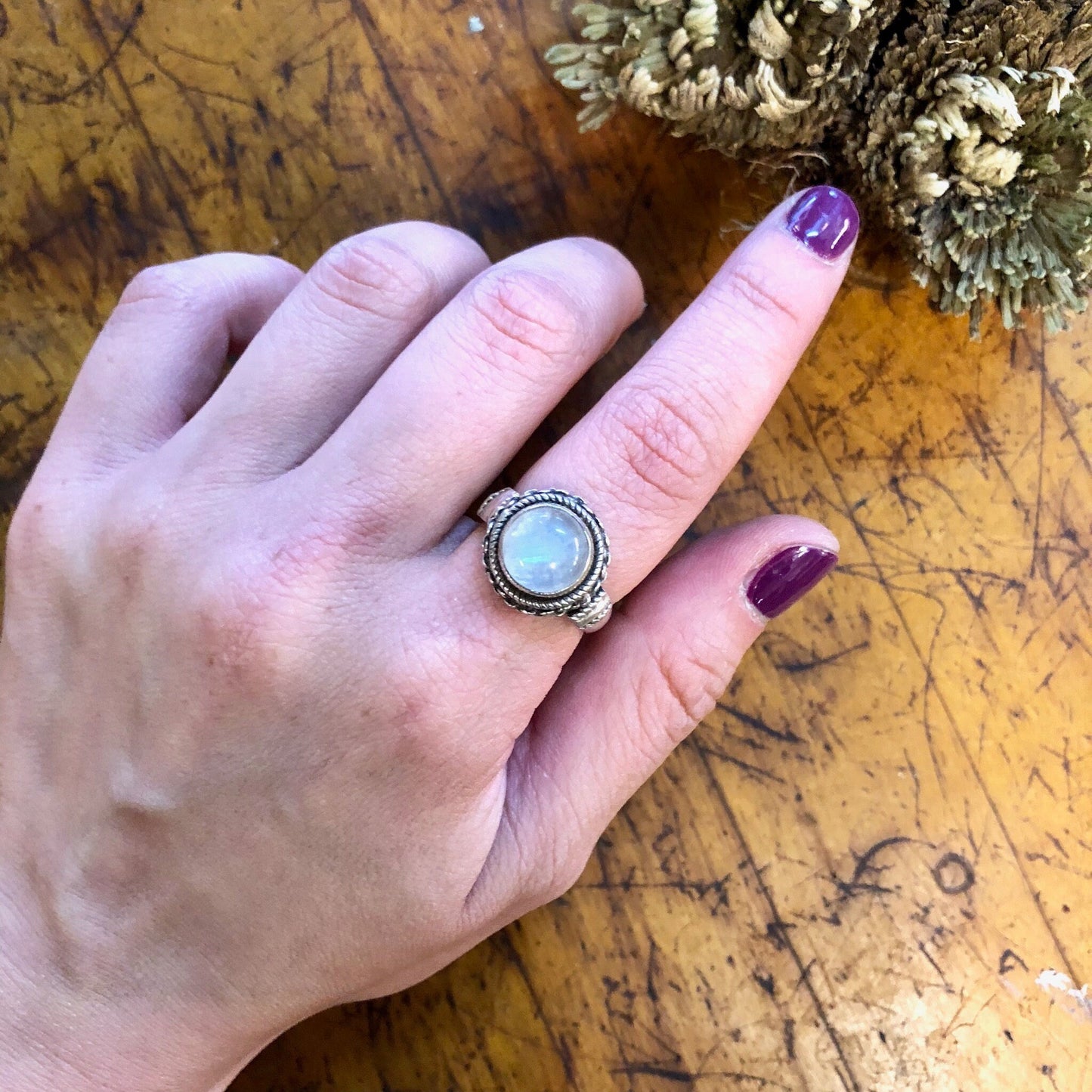 Vintage sterling silver moonstone ring with iridescent white stone on hand against wooden background