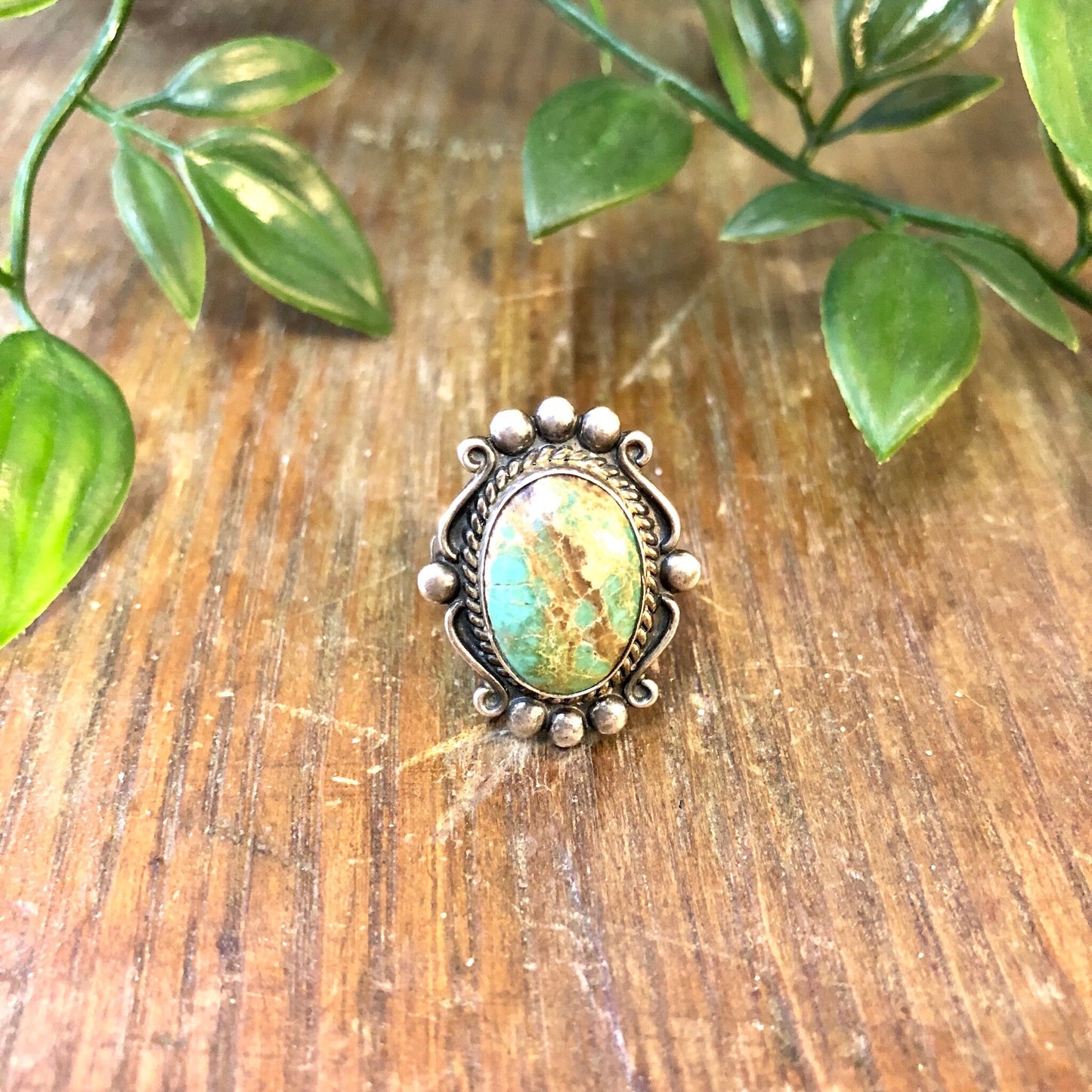 Vintage sterling silver ring with blue Royston turquoise cabochon on wooden surface with green leaves