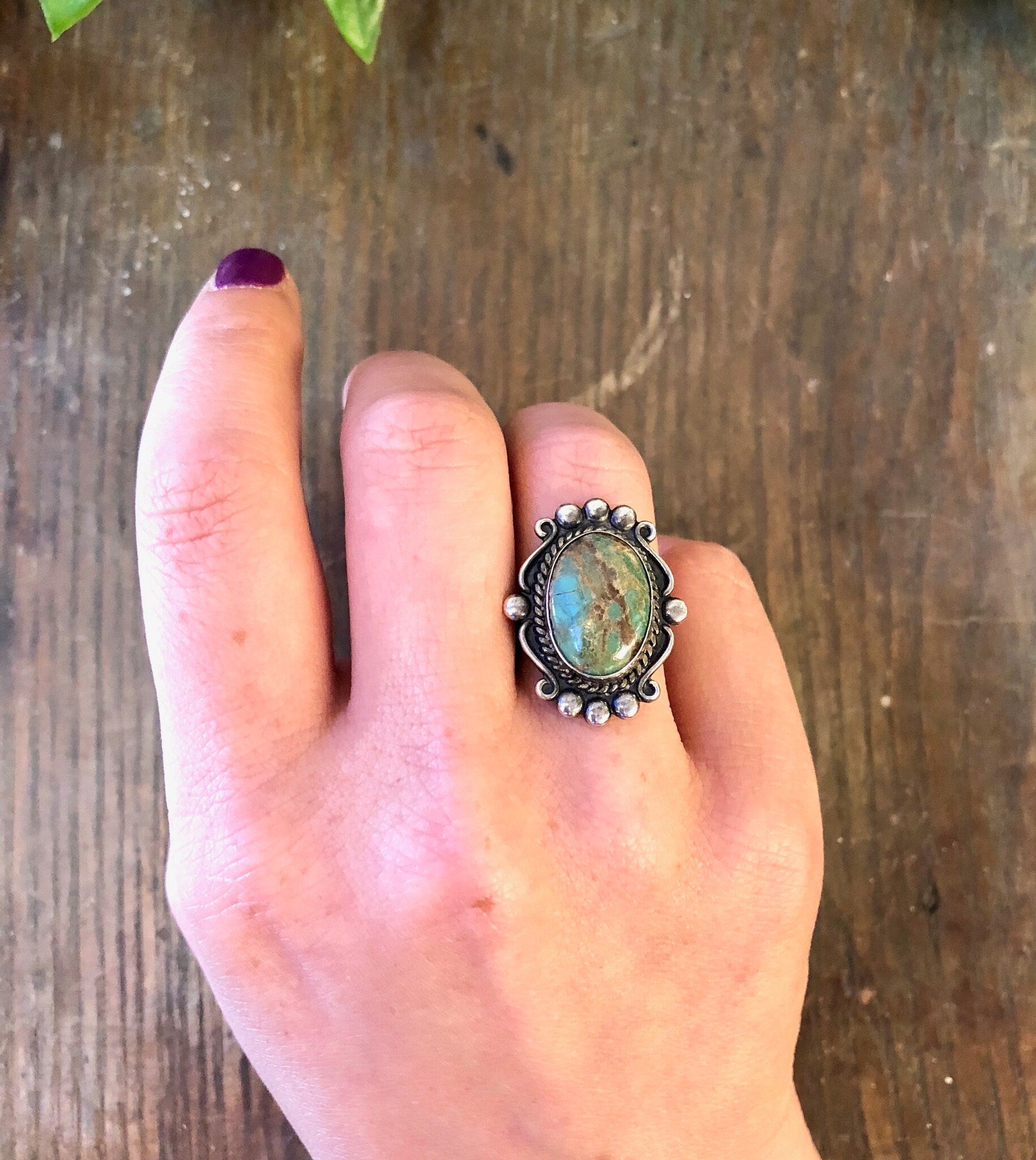 Vintage sterling silver ring with blue Royston turquoise cabochon on a person's hand against a wooden background.