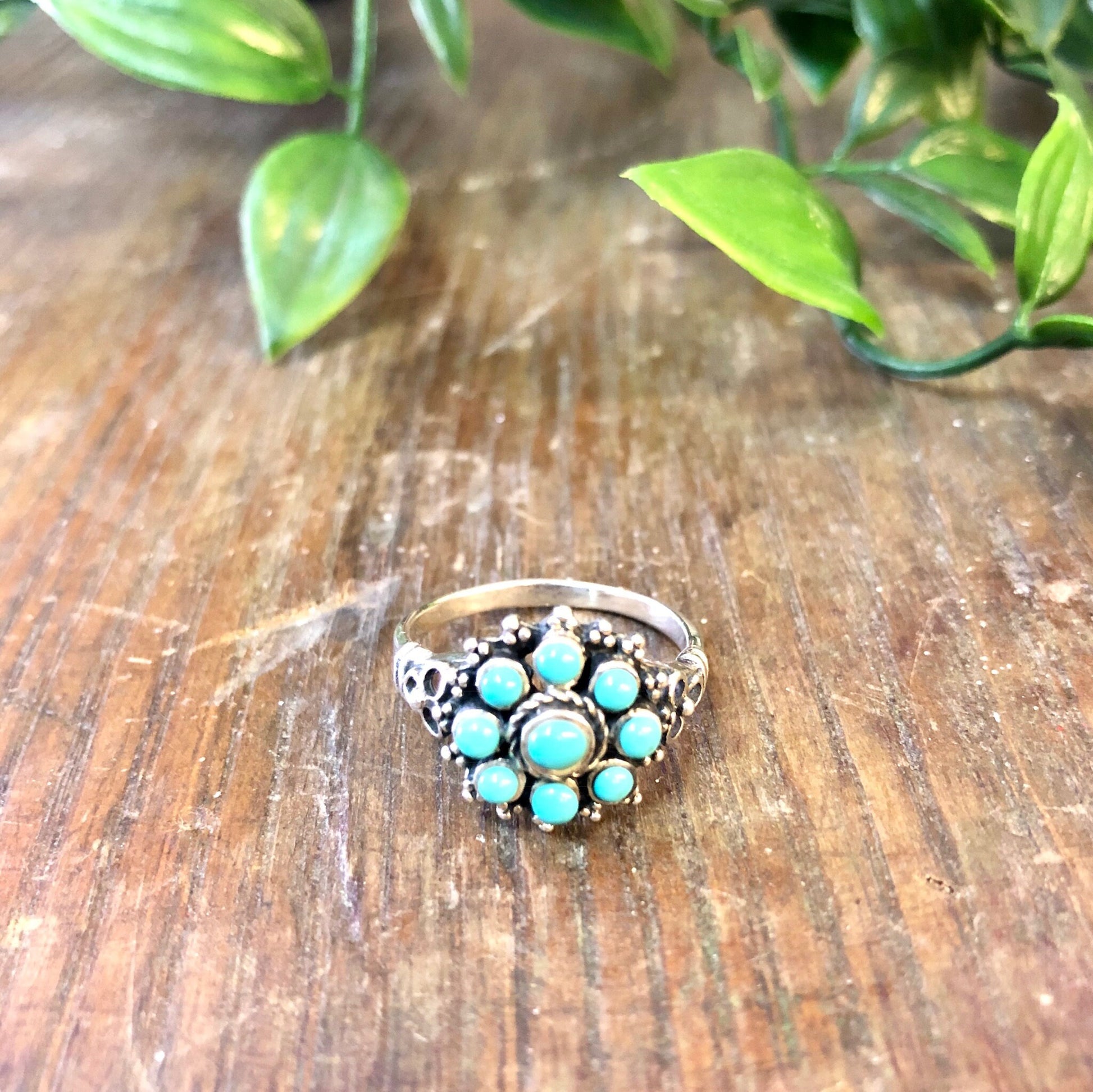 Vintage sterling silver ring featuring a flower-shaped cluster of turquoise beads set against a wooden surface with green leaves in the background