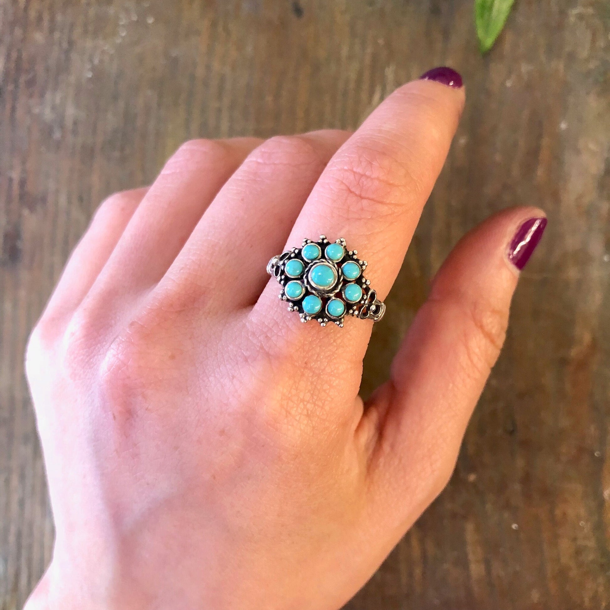 Vintage silver ring with turquoise beads on a finger, set against a wooden background with a leaf nearby