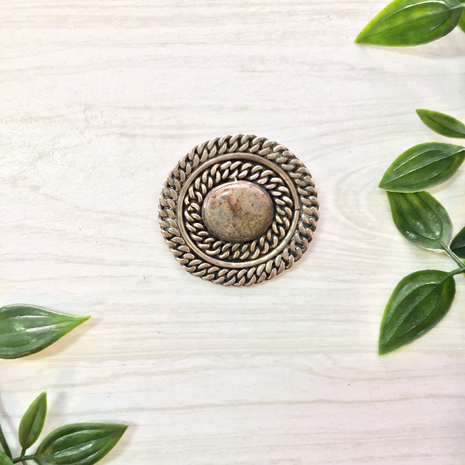 Vintage sterling silver Taxco brooch with round natural stone center, surrounded by green leaves on white wooden background, perfect gift for mom or vintage jewelry collector.