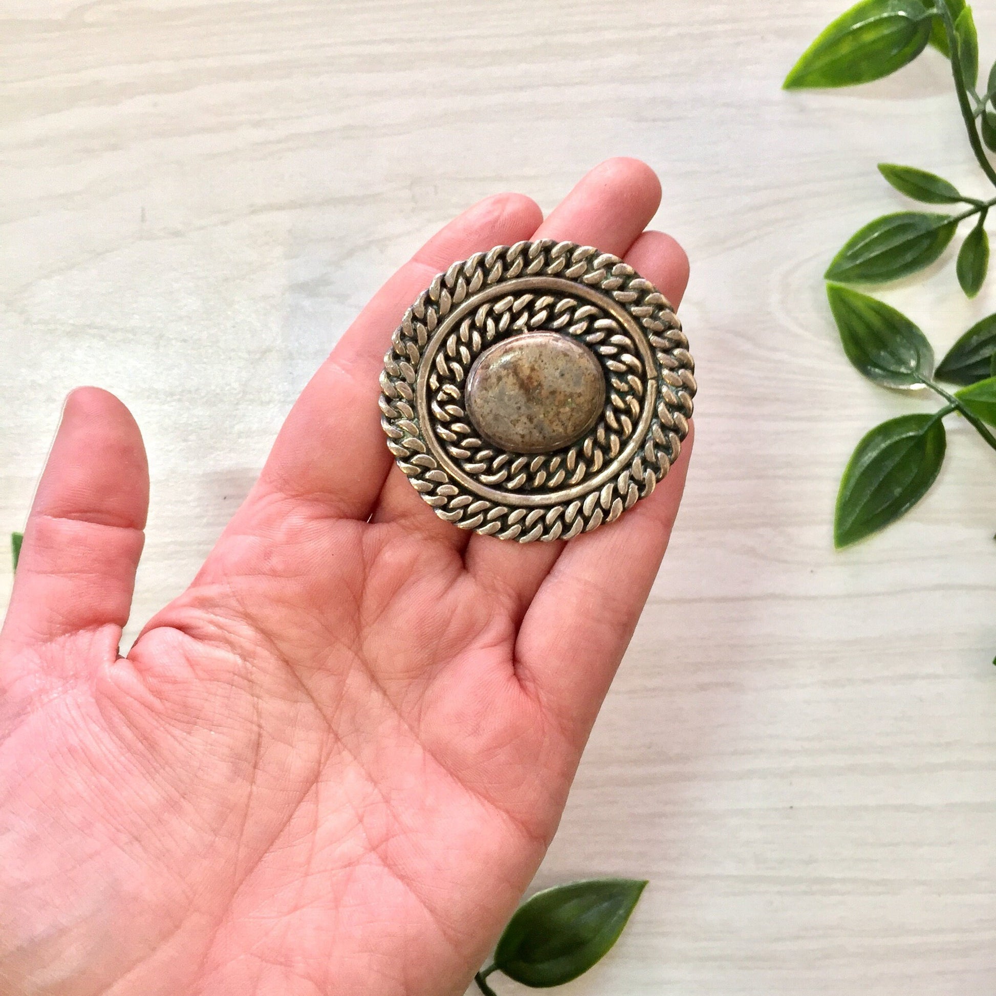 Vintage silver brooch with natural stone set in intricate round sterling silver design, handcrafted Taxco jewelry piece held in palm of hand with green leaves in background, perfect gift for Mom or vintage jewelry collector.