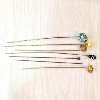 Vintage hat pins in various colors including blue, yellow, gold, black and white, displayed on a wooden surface. Collectible stick pins or scarf pins, suitable as a gift.