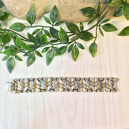 Vintage silver tone link bracelet with leaf design on wooden surface next to green foliage