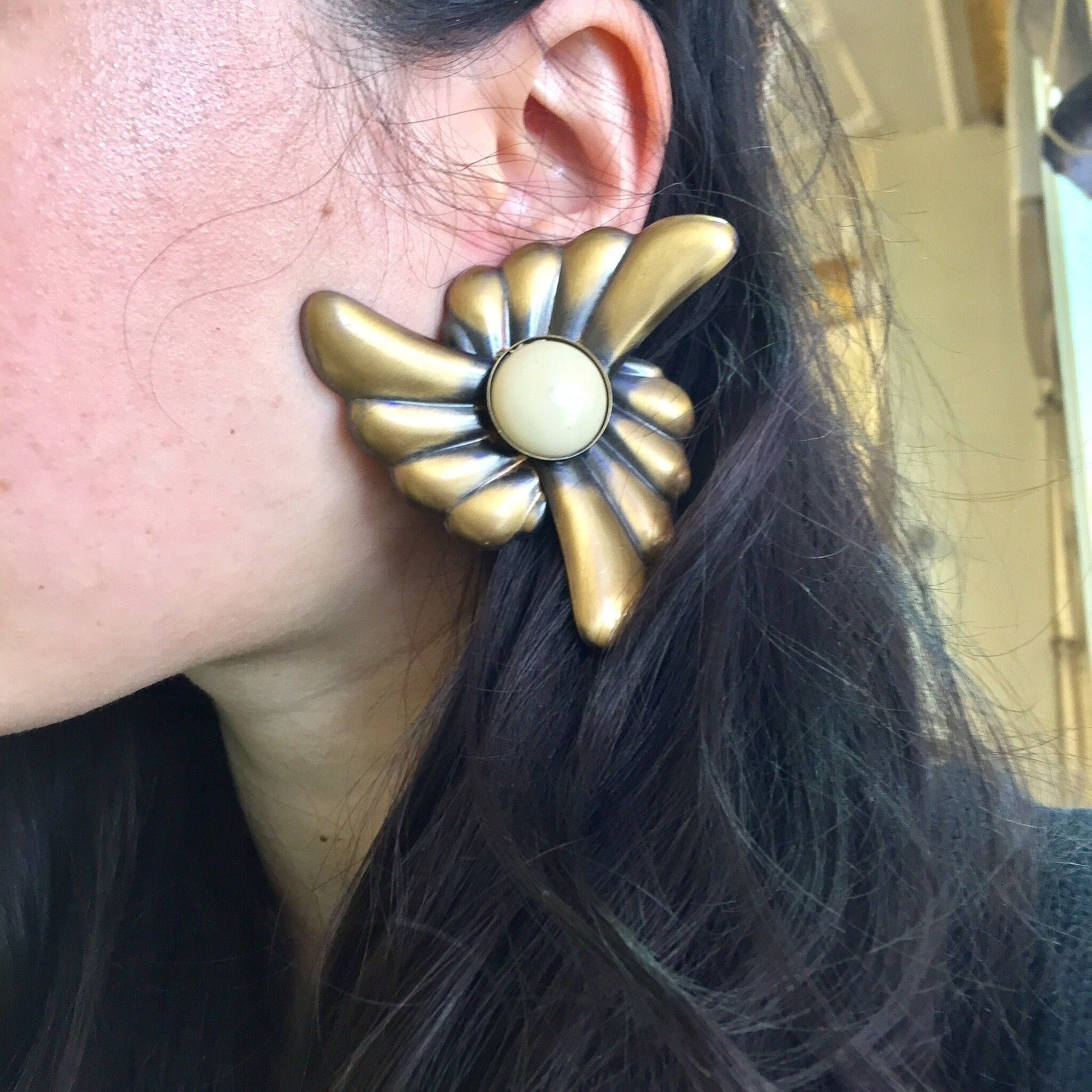 Vintage gold and white flower clip-on earrings on model's ear, with long dark hair visible. Large statement jewelry piece in a retro style.