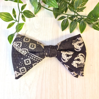 Vintage black bowtie with ornate white paisley pattern, clipped to foliage on wooden surface