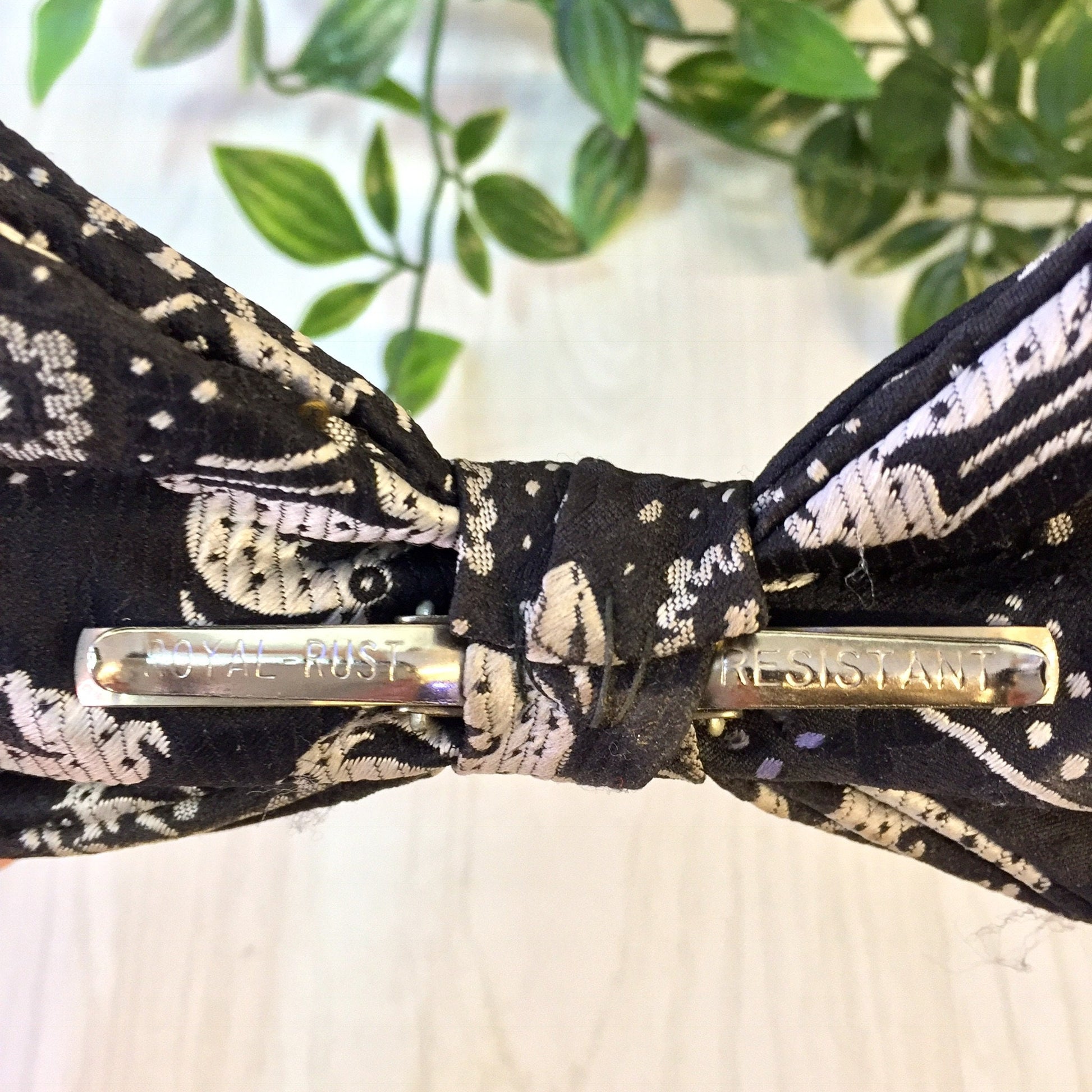 Vintage black patterned clip-on bow tie with "Resist" text on front, displayed with green foliage in background