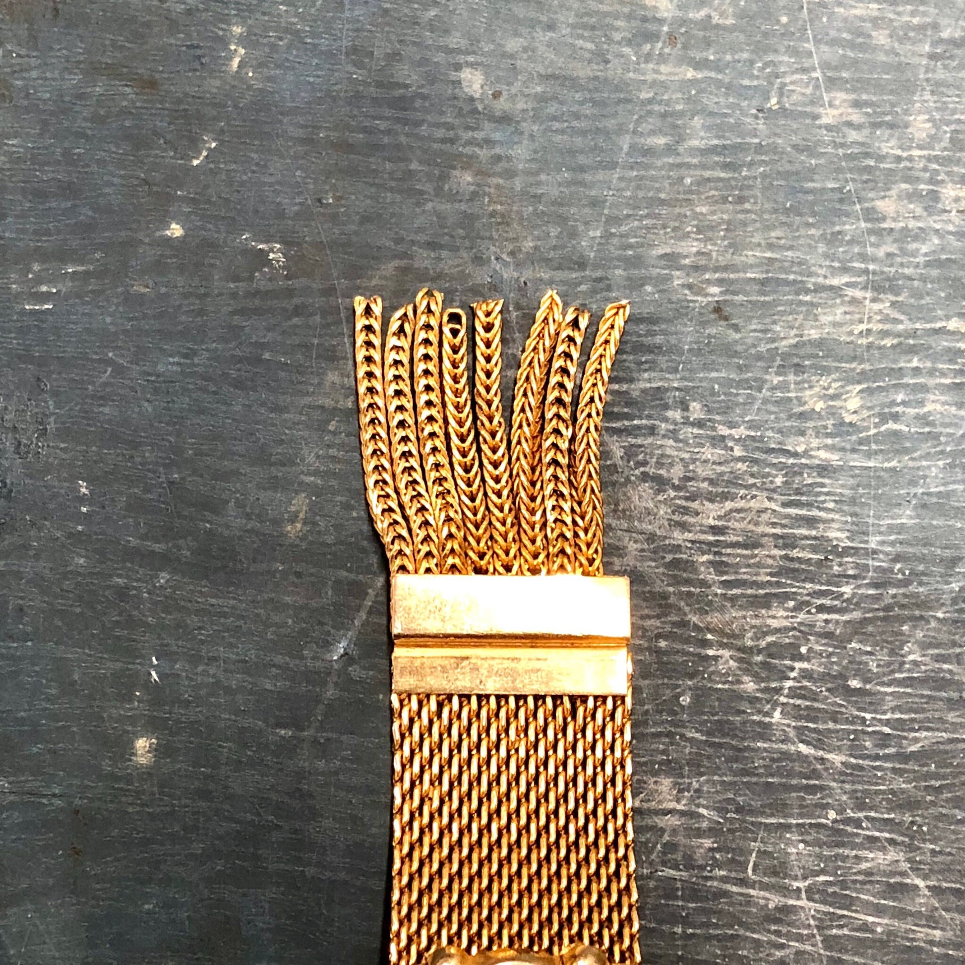 Vintage gold-toned tassel link bracelet on weathered gray wood surface