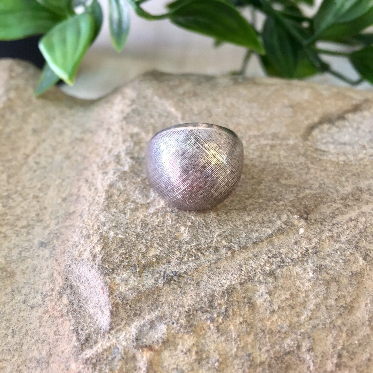 Vintage textured sterling silver pinky ring on stone surface with green leaves