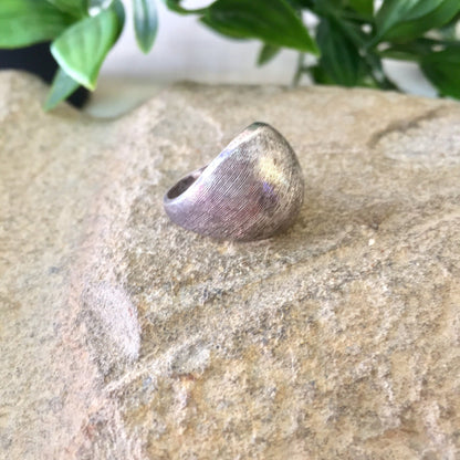 Vintage sterling silver textured pinky ring resting on stone surface with plant leaves in background