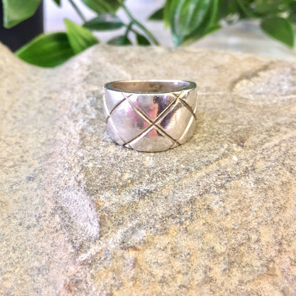 Vintage sterling silver thick band ring with crisscross X design and diamond pattern, displayed on sand with greenery in background, perfect as statement jewelry or gift.