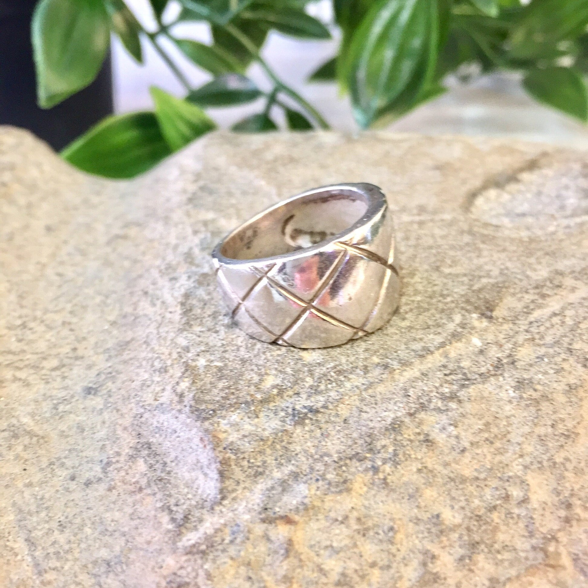 Vintage sterling silver ring with thick band and crisscross X design pattern, displayed on stone surface with greenery in background.