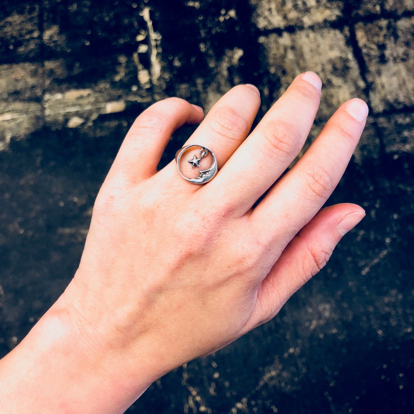 Vintage silver moon and star cutout ring on hand against weathered wooden background