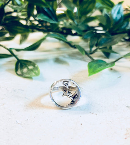 Vintage sterling silver moon and star cutout ring on white marble surface with green foliage in background